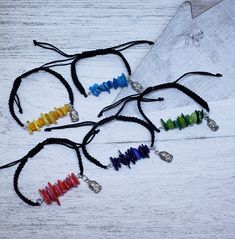 four bracelets with different colored beads are on a white wooden table next to a piece of fabric