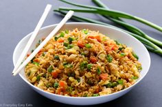 a white bowl filled with rice and veggies next to chopsticks on a table