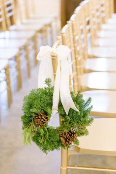 a wreath is tied to the back of a chair with pine cones and white ribbon