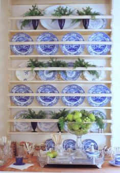 blue and white plates are stacked on a shelf with greenery in front of them