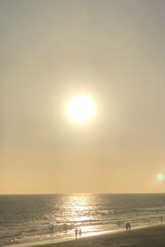 the sun is setting over the beach with people on it