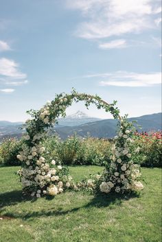 a wedding arch with white flowers and greenery in the foreground, overlooking mountains