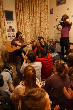 a group of people sitting in front of a man holding a guitar and singing into a microphone