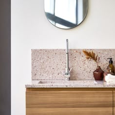 a bathroom sink sitting under a mirror next to a wooden cabinet and wall mounted faucet