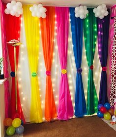 a room decorated with balloons, streamers and rainbow colored drapes on the wall