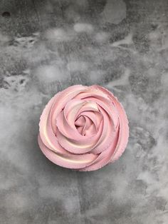 a pink cupcake sitting on top of a gray table next to white frosting