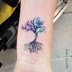 a small tree tattoo on the wrist with watercolor splashes and roots growing out of it