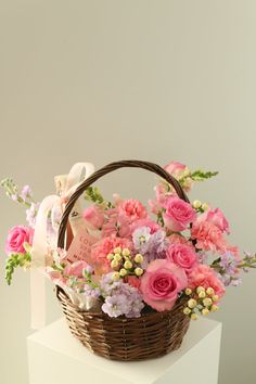 a basket filled with pink and purple flowers on top of a white pedestal next to a wall