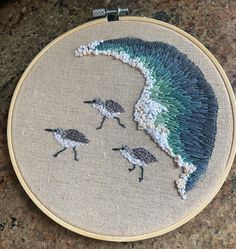 an embroidery project with three birds on the sand and one is flying in the air