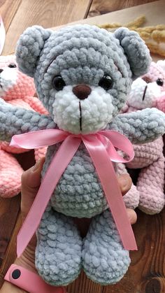 a hand holding a gray teddy bear with pink ribbon around it's neck and two other crocheted bears in the background