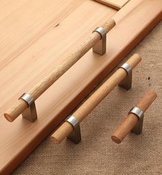 two wooden handles and one metal handle on a piece of wood next to a pair of pegs