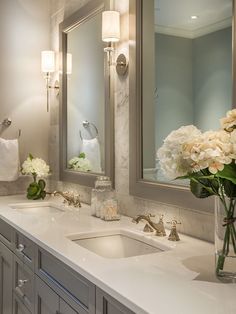 a bathroom with two sinks and a large mirror on the wall next to flowers in a vase