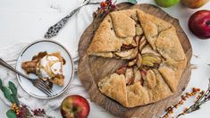 an apple pie on a wooden cutting board next to some apples and other food items