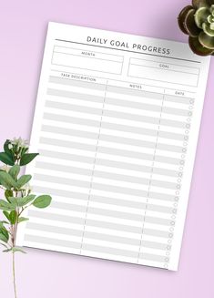 a daily goal sheet next to a potted plant on a pink background with copy space