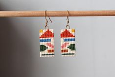 two pairs of beaded earrings hanging from a wooden hanger on a gray wall