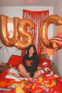 a woman sitting on top of a bed surrounded by balloons and other items in front of her