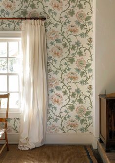 a chair sitting in front of a window next to a wall papered with flowers