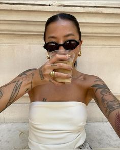 a woman with tattoos holding a glass of wine in front of her face and looking at the camera