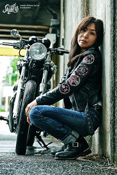 a woman sitting next to a motorcycle leaning against a wall with her hand on the ground