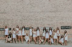 a group of women in white dresses standing next to each other near a brick wall