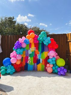 an arch made out of balloons and streamers in the middle of a backyard area