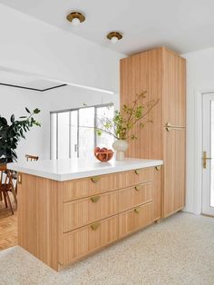 a kitchen with white counter tops and wooden cabinets in front of a large potted plant