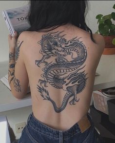 a woman with a dragon tattoo on her back holding a book in front of her