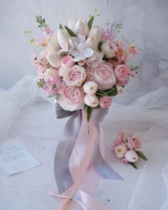 a bridal bouquet with pink and white flowers in it on a table next to a card