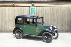 an old green car parked in front of a wooden building