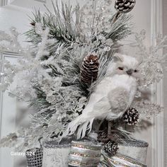 a white bird sitting on top of a christmas tree with pine cones and tinsel