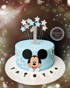 a blue cake with white stars and mickey mouse topper on it's side