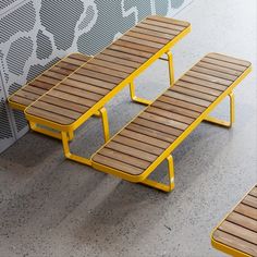 three wooden benches sitting next to each other on cement floored area with wall in background