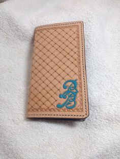 a brown wallet with blue lettering on it sitting on top of a white towel next to a cell phone