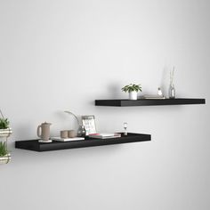 two black floating shelves with plants and books on them in front of a white wall