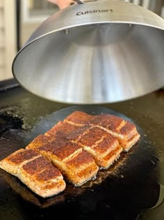 two pieces of toasted bread are being cooked on a griddle with a frying pan in the background