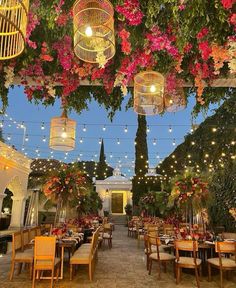 an outdoor dining area with tables and chairs, hanging lights and flowers on the ceiling