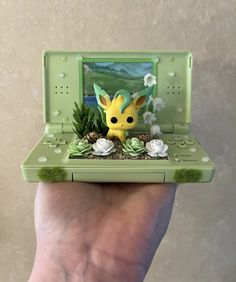 a hand holding a small toy laptop with a pikachu figure on it