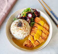 a white plate topped with rice and meat next to chopsticks