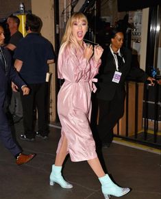 a woman in a pink raincoat and blue boots is walking down the street with her mouth open