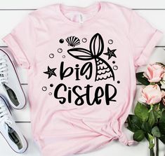 a pink shirt with the words big sister on it next to some flowers and a pair of sneakers