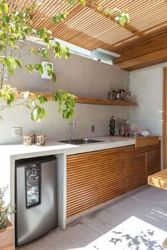 an outdoor kitchen with wooden cabinets and counter tops, under a pergolated roof