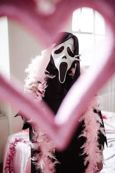 a person wearing a mask and pink feathers in front of a heart shaped frame with the face of a ghost