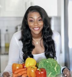 a woman sitting at a table with vegetables and fruit in front of her, smiling