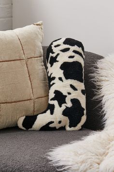 a cow print pillow sitting on top of a couch next to a black and white throw pillow