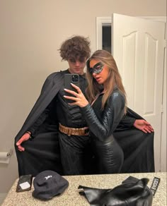 a man and woman dressed up as batman and catwoman taking a selfie in front of a mirror