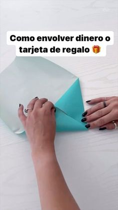 a woman cutting paper with scissors on top of a white table next to a blue piece of paper