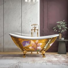 an ornate bathtub with flowers painted on the side and gold faucet, next to a potted plant