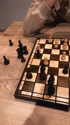 a man sitting at a table with chess pieces scattered around him on the wooden floor