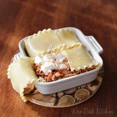 a casserole dish filled with meat and cheese on a wooden table next to coins