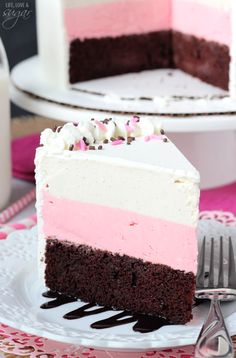 a slice of cake with pink, white and chocolate frosting on a plate next to a fork